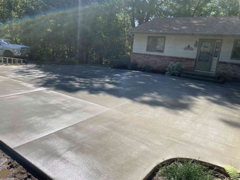 Freshly poured concrete driveway with a residential home in the background and trees nearby.