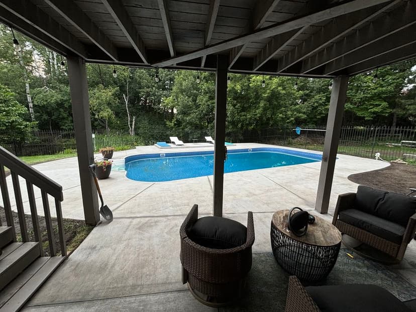 View of a serene backyard pool area with seating and lush greenery in the background.