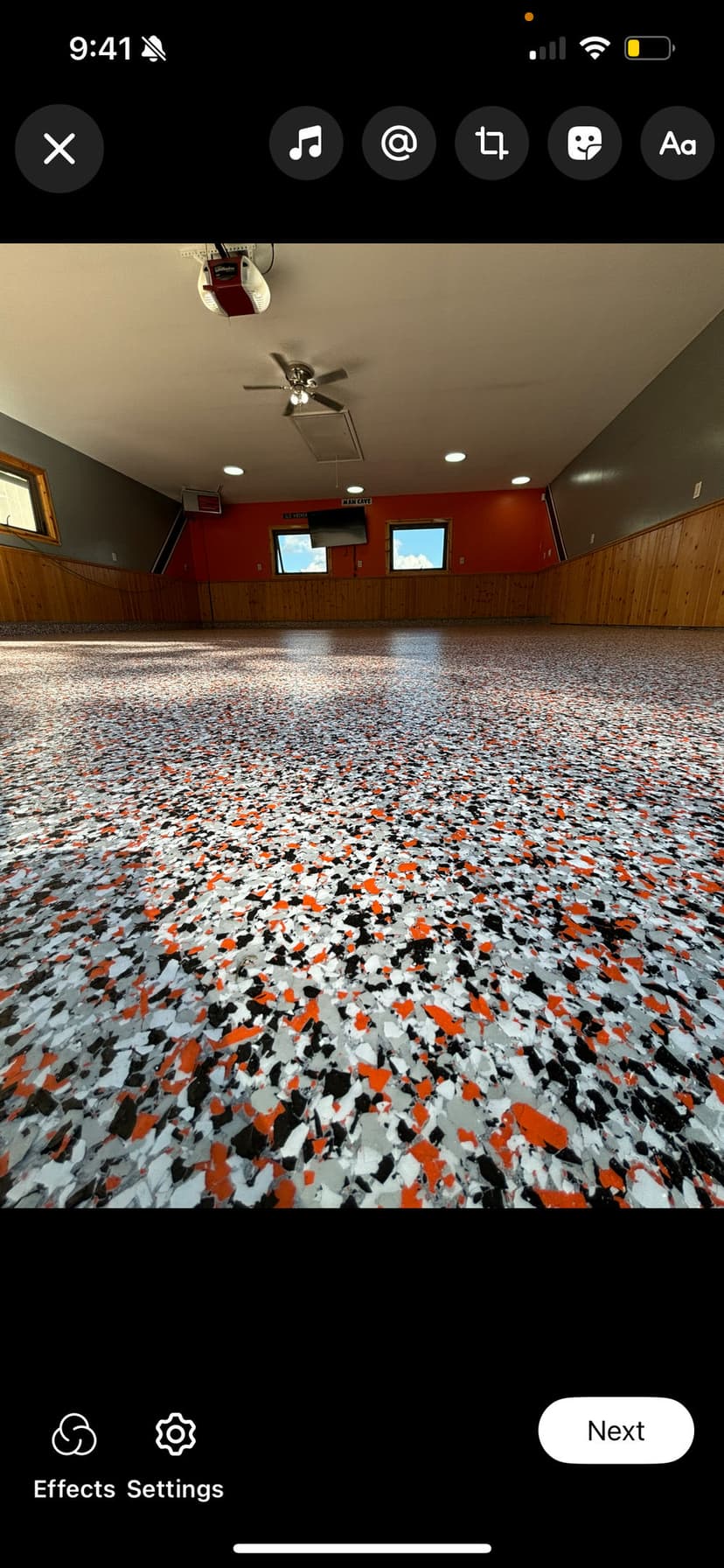 Epoxy floor with black, orange, and white speckles in a spacious room with wooden walls.