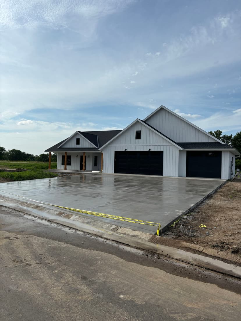 Newly constructed modern home with a concrete driveway and black garage doors under a blue sky.
