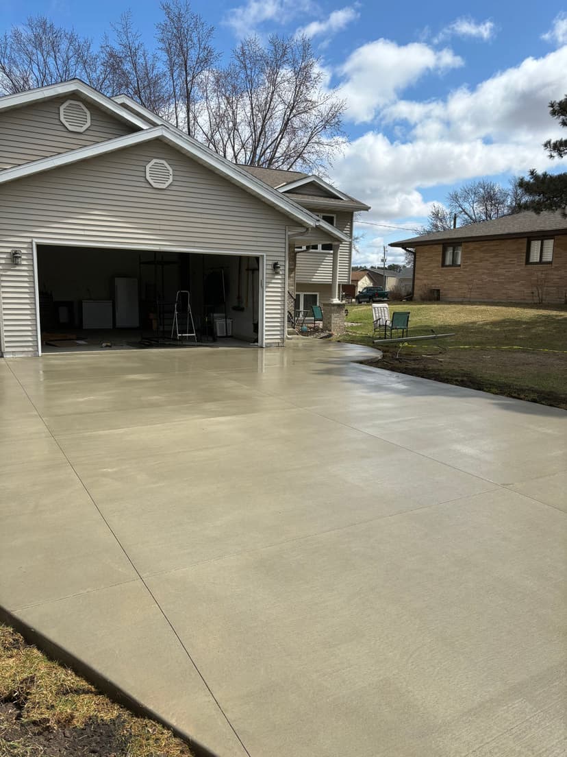 Freshly poured concrete driveway in front of a residential garage on a sunny day.